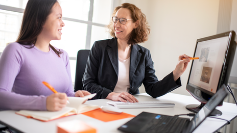 Photo of a student and an employee of the scholarship advisory service. They are sitting at a table. The employee points to something on the laptop and they talk.