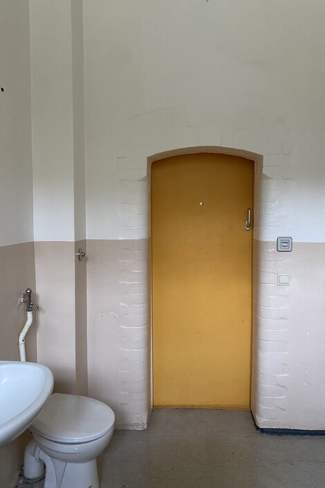 Blick aus der Gefängniszelle auf die verschlossene Tür und die Toilette