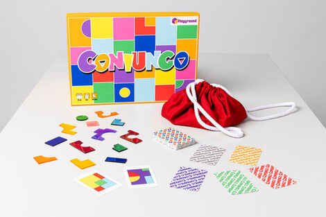 Auf einem Tisch liegen farbige Puzzleteile, Spielkarten, eine Schachtel und ein Stoffsack.