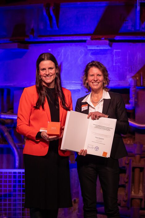 Two women stand next to each other, smiling and facing the camera.
On the left is Celine Carstensen-Opitz, holding an organ-colored cube with the inscription 2023. To the right is Prof. Dr. Nicole Knuth, who is presenting her certificate for the 2023 Award of the Dortmund University of Applied Sciences and Arts for special achievements in research and development.