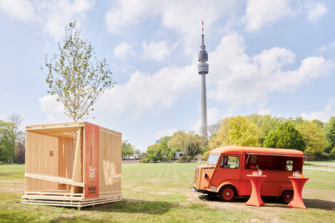 A wooden construction in the shape of a cube stands on a meadow.