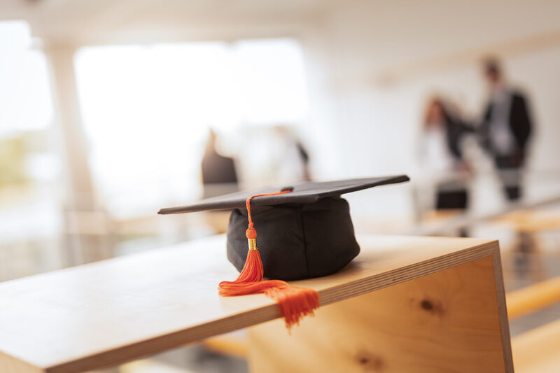 Photo of a doctor's hat on a wooden shelf. People are recognizable in the background.