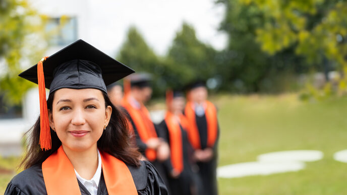 Photo of a young woman wearing a doctor's hat, smiling at the camera. Behind her, out of focus, are several people also wearing doctor's hats.