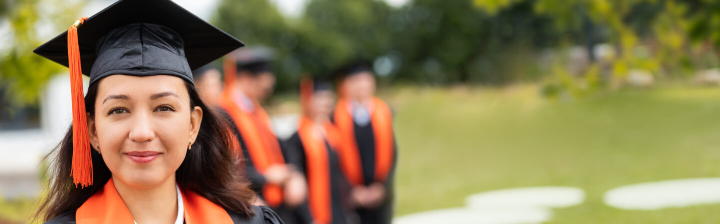 Photo of a young woman wearing a doctor's hat, smiling at the camera. Behind her, out of focus, are several people also wearing doctor's hats.