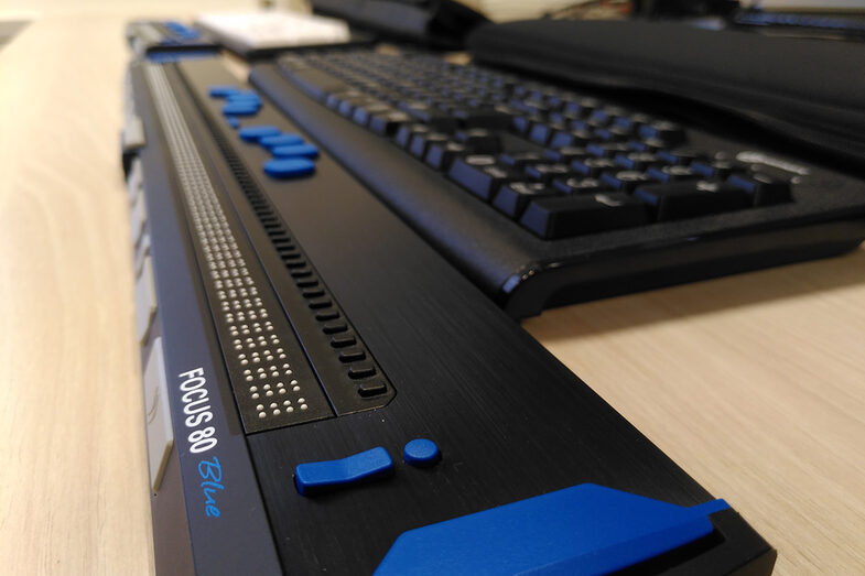 Detailaufnahme von einem Schreibtisch mit einer Tastatur und einer davorliegenden Braillezeile für ertastbare Punktschrift.