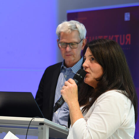 Photos of a lecture from the Faculty of Architecture. A woman speaks into a microphone, a man stands behind her.