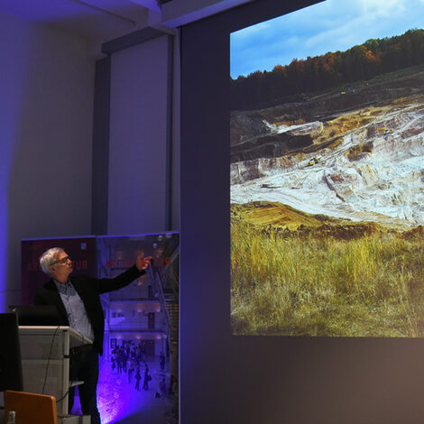 Fotos von einem Vortrag aus dem Fachbereich Architektur. Ein Mann steht vor einer Leinwand und zeigt dorthin.