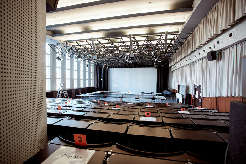 Foto mit Blick auf die Leinwand im Kinosaal, über die Stuhlreihen hinweg. __ View of the screen in the cinema, across the rows of chairs.