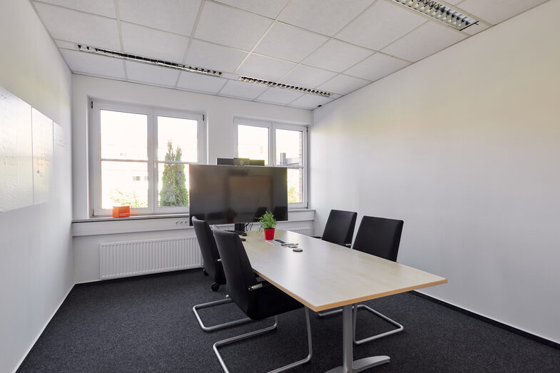 Room shot of a conference room with table, four chairs and digital board.