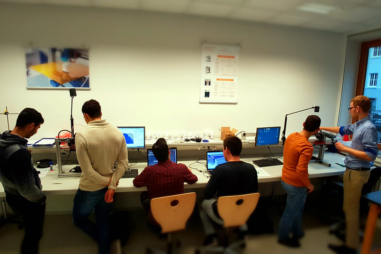 Photo of a group of people standing at the 3D printers and someone explaining something.