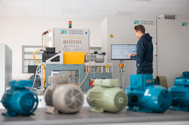 Foto von einem Elektromotorenprüfstand sowie einem Studierenden, der den Prüfstand bedient. Davor sind Motoren aufgereiht.