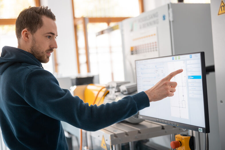 Foto von einem Studierenden an einem Elektromotorenptüfstand, wo er den dazugehörigen Monitor bedient.