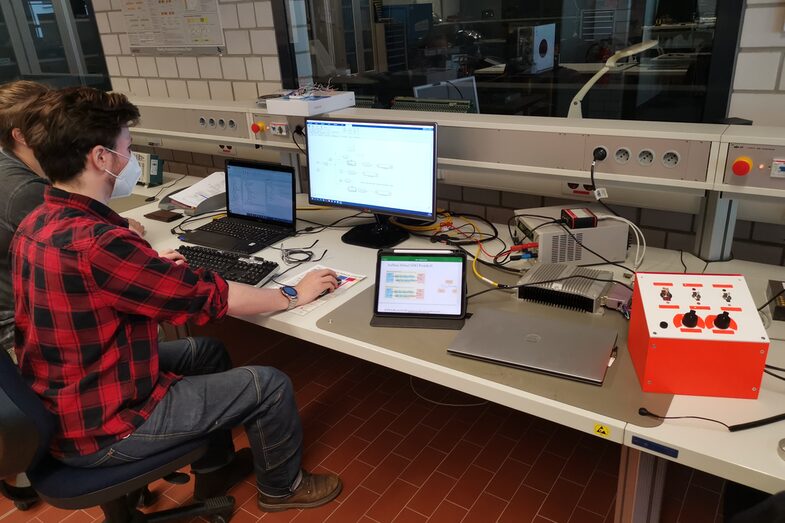 Foto von zwei Studierenden, die an einem Rechner sitzen und an einer MicroAutoBox 3 & MatLab/Simulink arbeiten.<br>