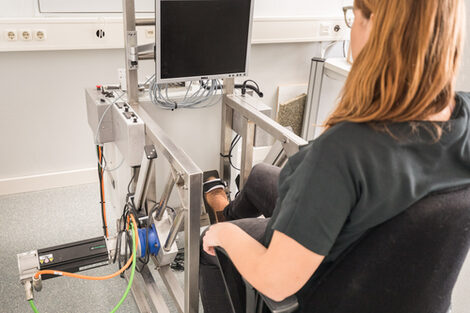 Foto einer Probandin im neurologischen Gerät mit Fußpedalen zum Hineinsetzen zur Vitaldatenerfassung nach Schlaganfall.