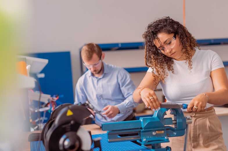 A man and a woman can be seen working at a workbench.